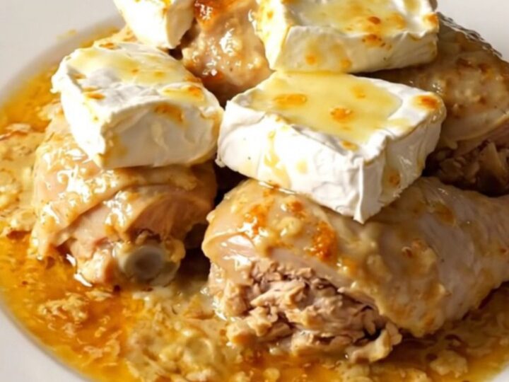 A top-down view of a black slow cooker filled with raw chicken, sliced onions, and slices of Camembert cheese.