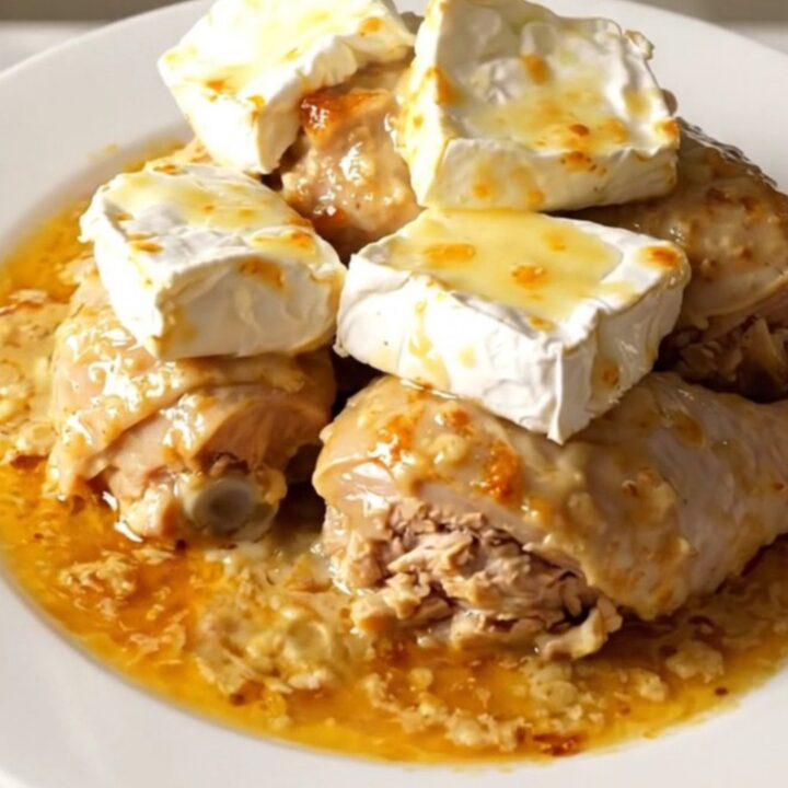 A top-down view of a black slow cooker filled with raw chicken, sliced onions, and slices of Camembert cheese.