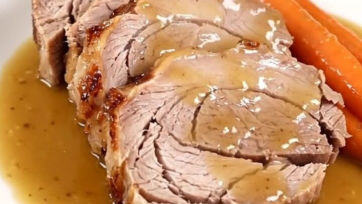 A slow-cooked pork roast with mustard, carrots, and onions in a slow cooker.