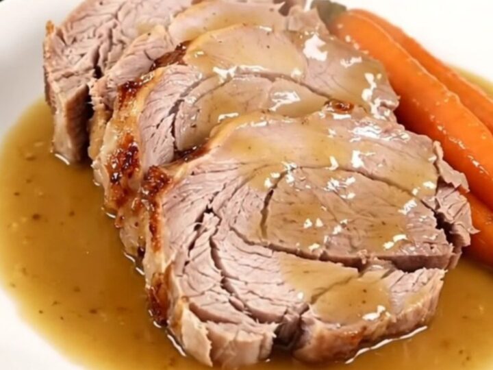 A slow-cooked pork roast with mustard, carrots, and onions in a slow cooker.