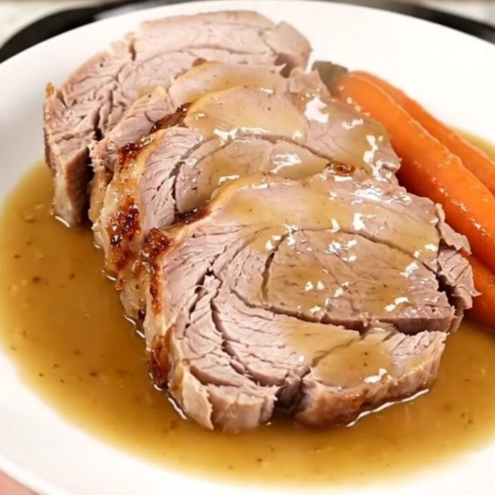 A slow-cooked pork roast with mustard, carrots, and onions in a slow cooker.