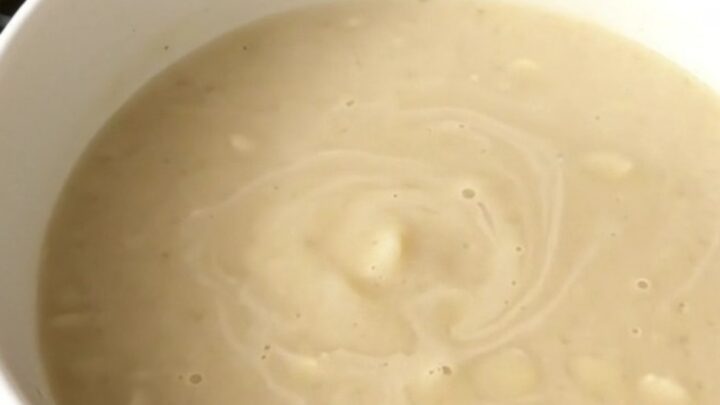 A top-down view of a black slow cooker filled with diced potatoes, garlic, and bouillon cubes before adding water.