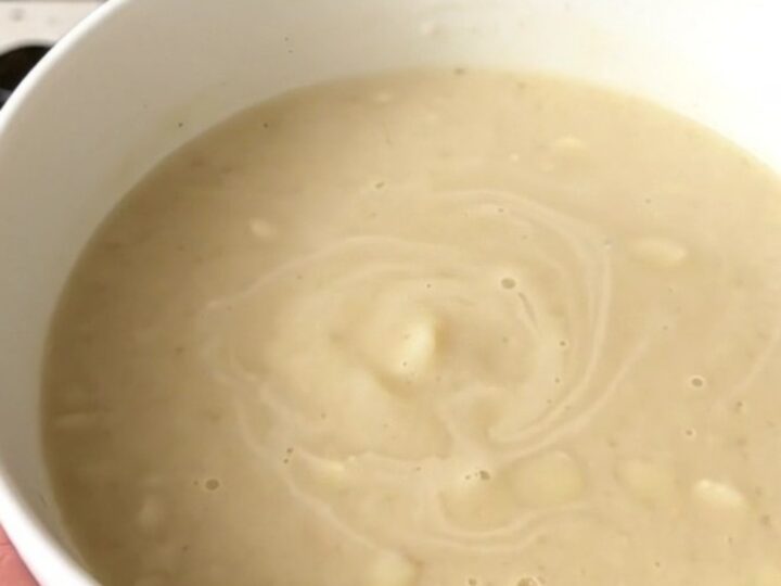 A top-down view of a black slow cooker filled with diced potatoes, garlic, and bouillon cubes before adding water.