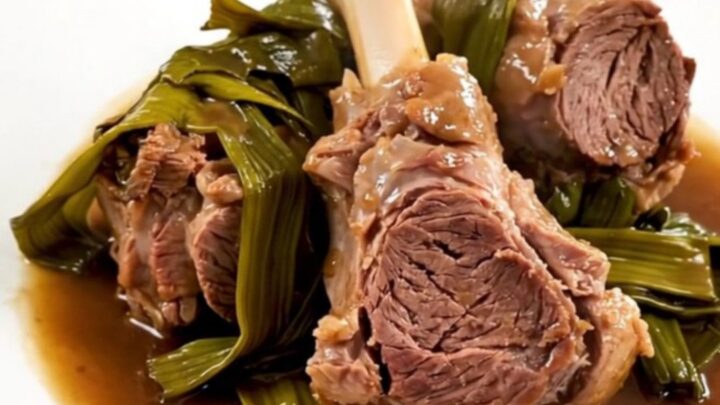 A top-down view of raw lamb chunks and sliced leeks in a black slow cooker on a white quartz countertop.