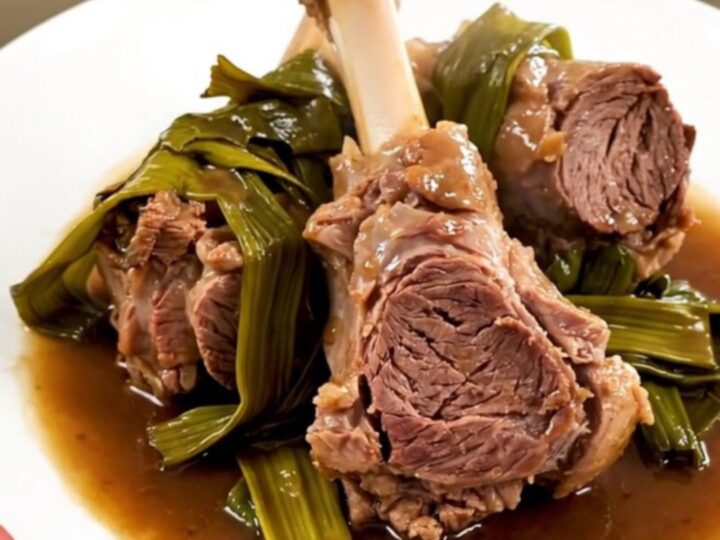 A top-down view of raw lamb chunks and sliced leeks in a black slow cooker on a white quartz countertop.