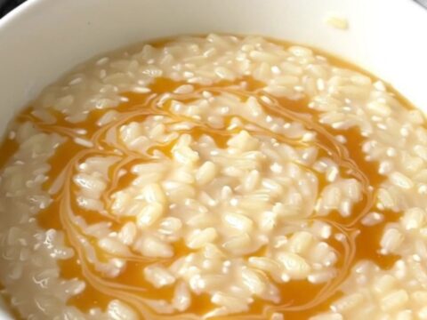 A top-down view of a black slow cooker filled with creamy rice pudding and golden swirls of caramel.