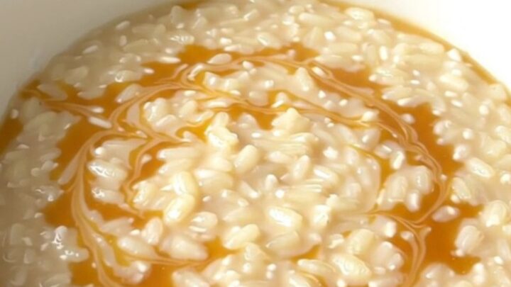 A top-down view of a black slow cooker filled with creamy rice pudding and golden swirls of caramel.