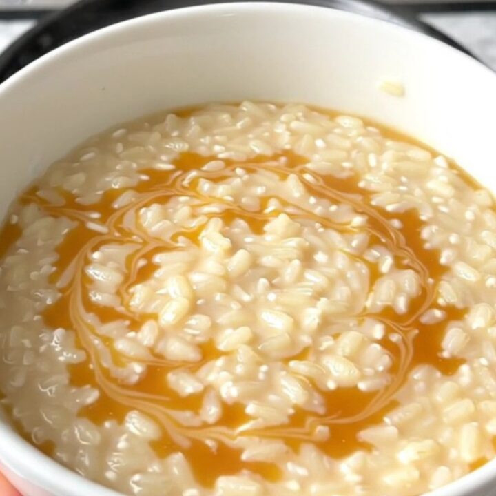 A top-down view of a black slow cooker filled with creamy rice pudding and golden swirls of caramel.