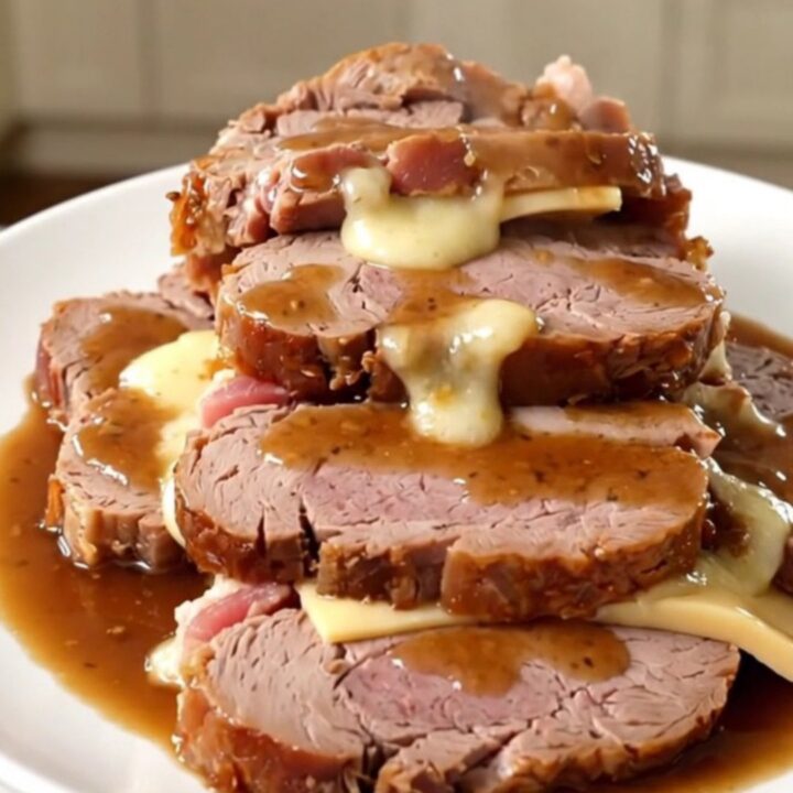 A slow cooker filled with a bacon and cheese stuffed veal roast surrounded by onions and herbs.