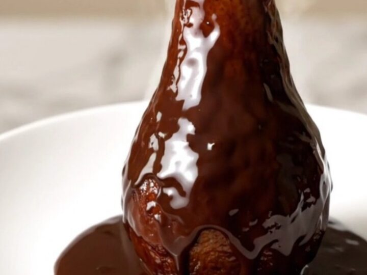 Poires entières pochées au chocolat noir brillant sur une assiette blanche.