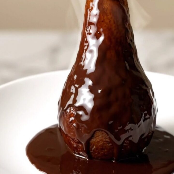 Poires entières pochées au chocolat noir brillant sur une assiette blanche.