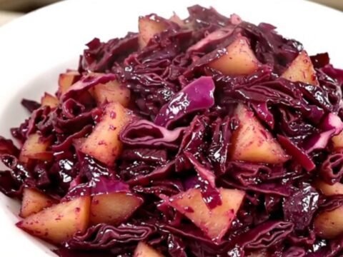 A top-down view of a slow cooker filled with shredded red cabbage and sliced apples.