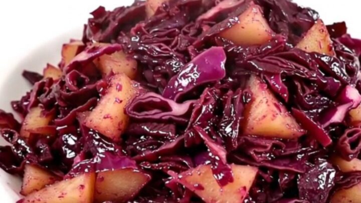 A top-down view of a slow cooker filled with shredded red cabbage and sliced apples.
