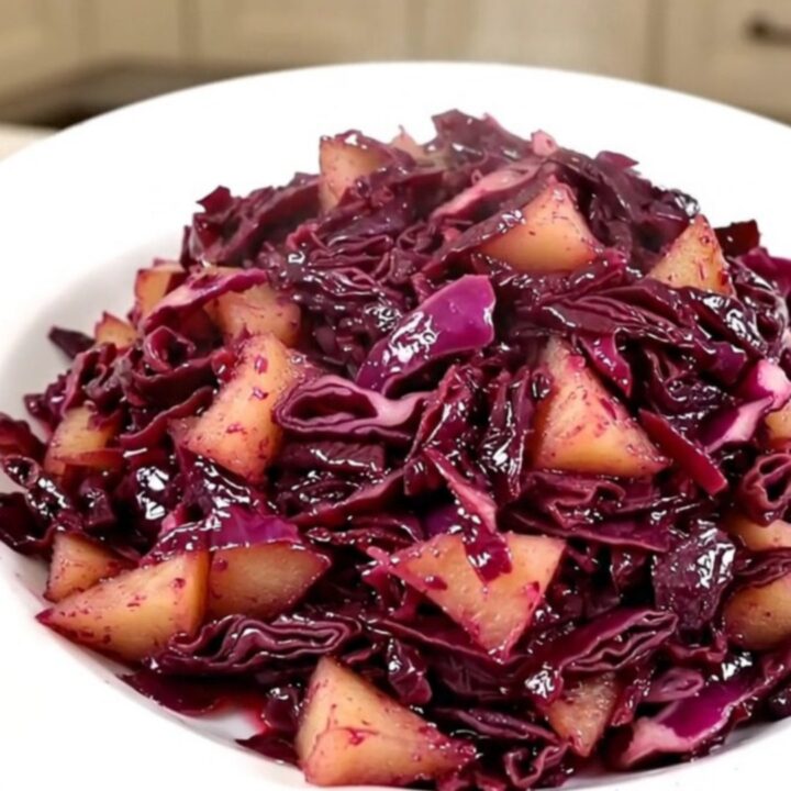 A top-down view of a slow cooker filled with shredded red cabbage and sliced apples.