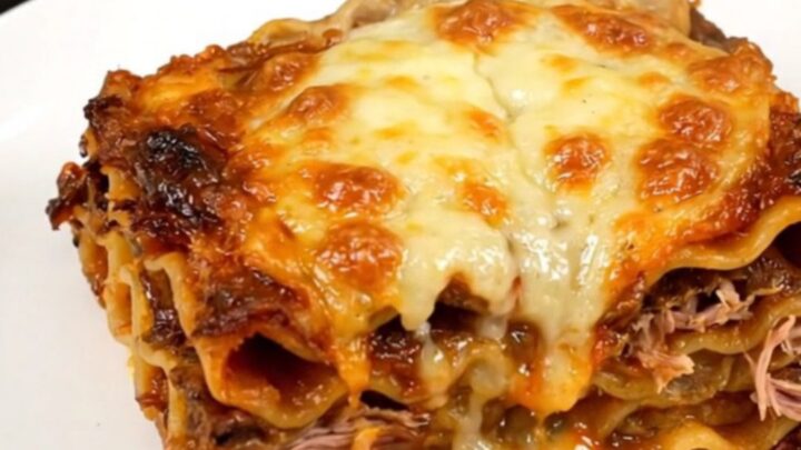 A top-down view of a black slow cooker filled with layers of lasagna, duck confit, mushrooms, and herbs.