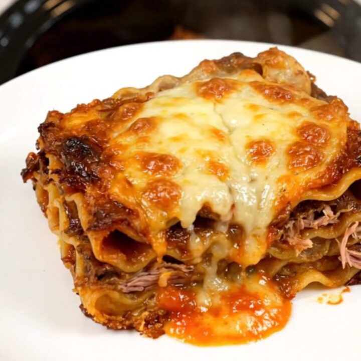 A top-down view of a black slow cooker filled with layers of lasagna, duck confit, mushrooms, and herbs.