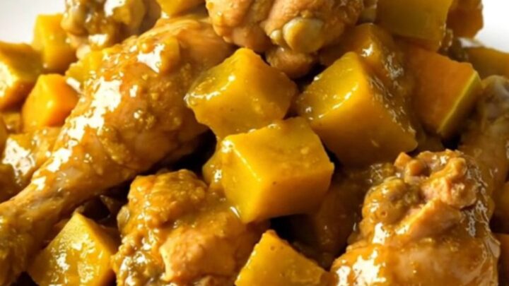 A steaming, glossy dish of slow cooker mild curry chicken with butternut squash on a white plate.