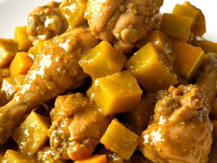 A steaming, glossy dish of slow cooker mild curry chicken with butternut squash on a white plate.