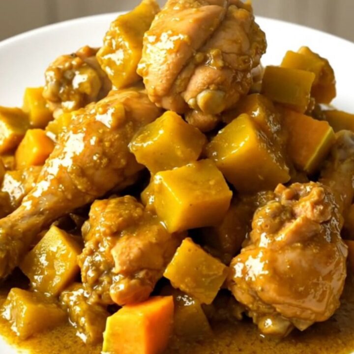 A steaming, glossy dish of slow cooker mild curry chicken with butternut squash on a white plate.