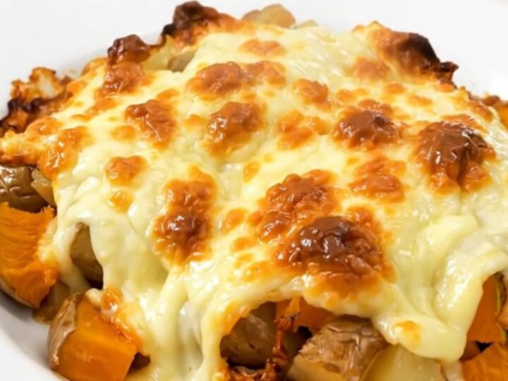 A close-up of a steaming, cheesy red kuri squash and potato gratin served on a plain white plate.