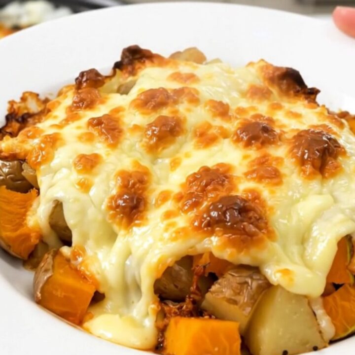 A close-up of a steaming, cheesy red kuri squash and potato gratin served on a plain white plate.
