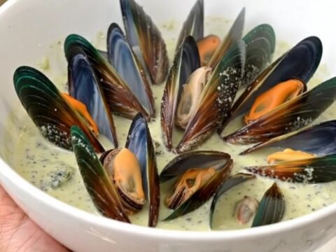 A top-down view of fresh mussels, shallots, Roquefort cheese, cream, and wine in a black slow cooker insert.