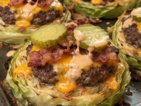 A close-up view of golden roasted cabbage rounds topped with juicy beef patties, crispy bacon, and melted cheddar.