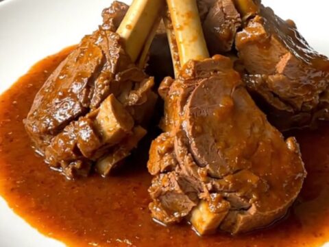 A top-down view of a black slow cooker filled with raw veal, sliced carrots, onions, and tomato coulis before cooking.