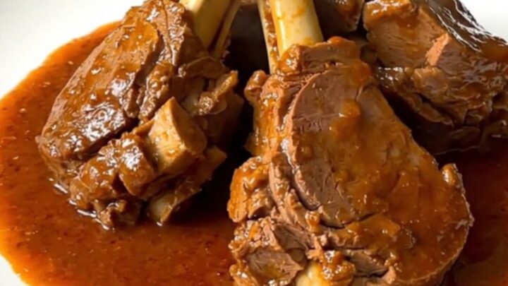 A top-down view of a black slow cooker filled with raw veal, sliced carrots, onions, and tomato coulis before cooking.