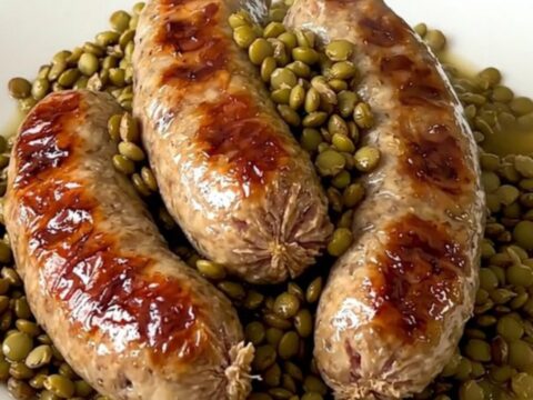 A top-down view of raw sausages, green lentils, and carrots being arranged in a slow cooker.