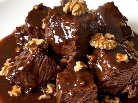 A close-up of glossy, tender beef daube with walnuts in a rich red wine sauce inside a slow cooker.