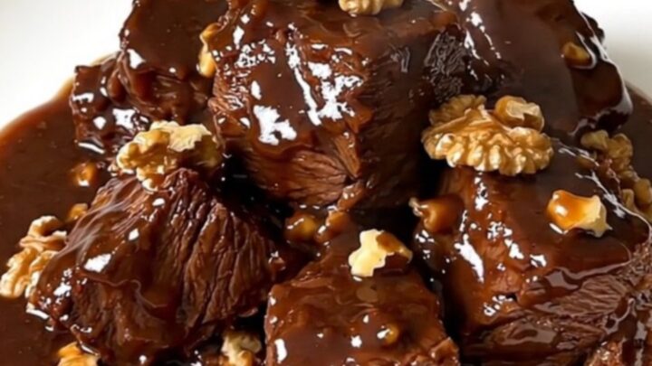 A close-up of glossy, tender beef daube with walnuts in a rich red wine sauce inside a slow cooker.