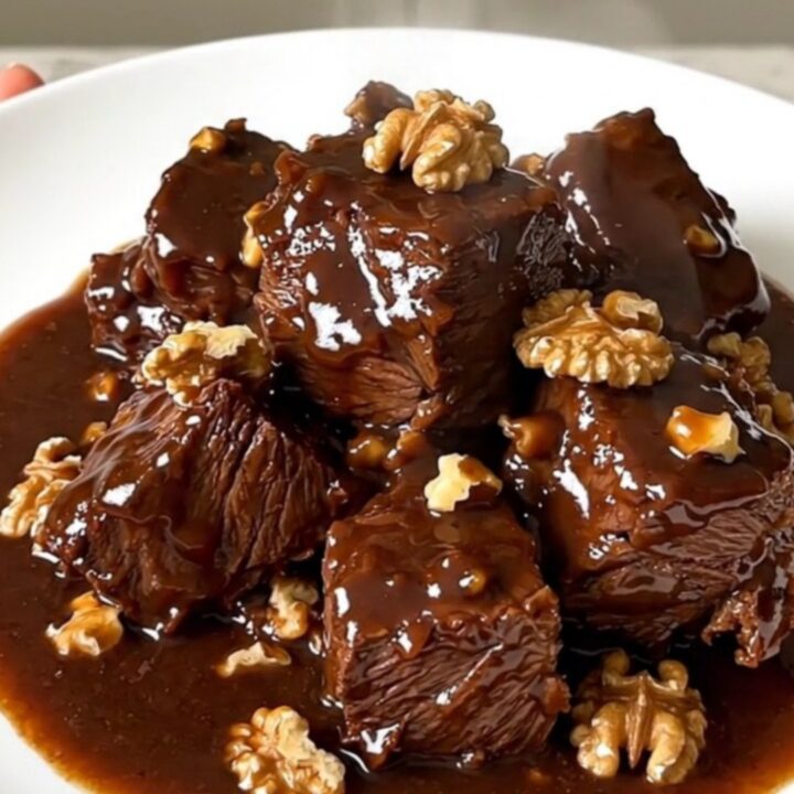 A close-up of glossy, tender beef daube with walnuts in a rich red wine sauce inside a slow cooker.