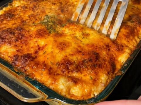 A close-up view of baked lasagna in a glass dish with a golden, bubbling cheese crust.