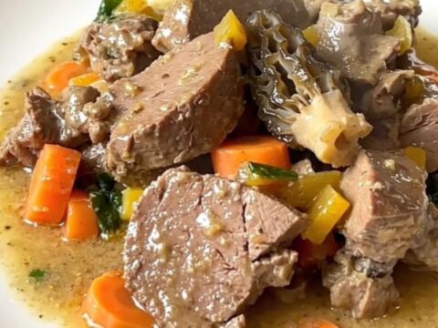 A steaming bowl of veal blanquette with carrots and morel mushrooms in a creamy sauce.