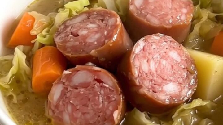A rustic bowl of cabbage and Morteau sausage soup with visible chunks of potato and sausage in a steaming, savory broth.