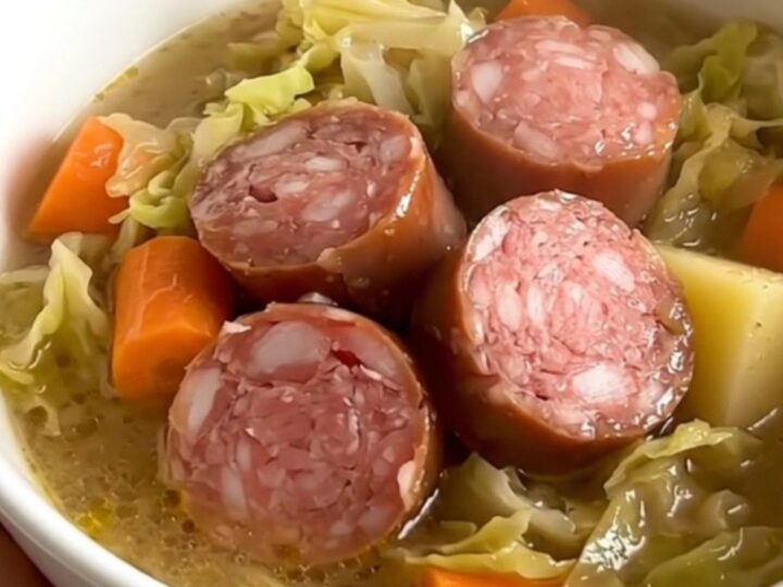 A rustic bowl of cabbage and Morteau sausage soup with visible chunks of potato and sausage in a steaming, savory broth.