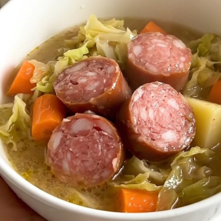 A rustic bowl of cabbage and Morteau sausage soup with visible chunks of potato and sausage in a steaming, savory broth.