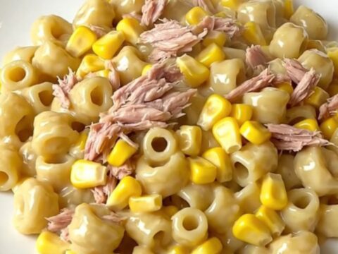 A top-down view of a black slow cooker filled with uncooked ingredients like tuna, corn, and pasta.