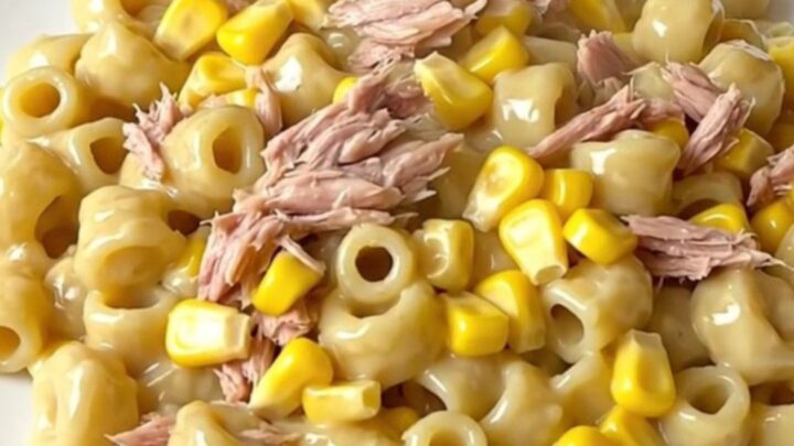 A top-down view of a black slow cooker filled with uncooked ingredients like tuna, corn, and pasta.