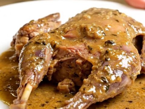 A close-up of tender, slow-cooked rabbit served in a creamy garlic and thyme sauce on a white plate.