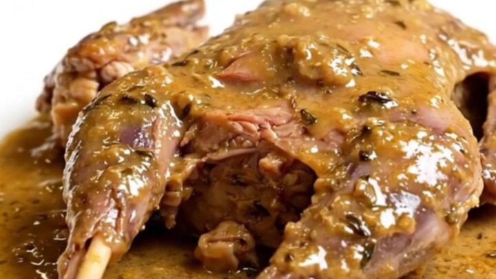 A close-up of tender, slow-cooked rabbit served in a creamy garlic and thyme sauce on a white plate.
