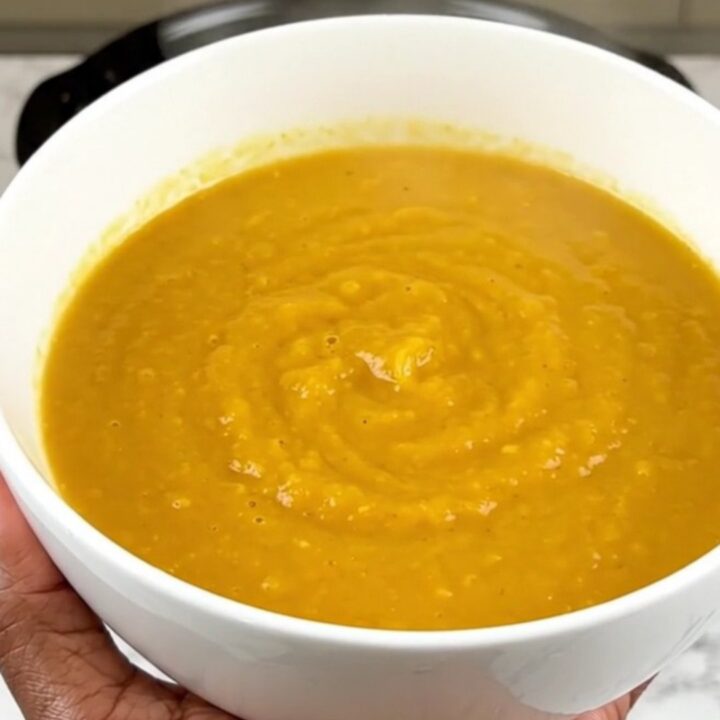 A steaming bowl of vibrant orange carrot, orange, and coriander soup on a white speckled quartz countertop.