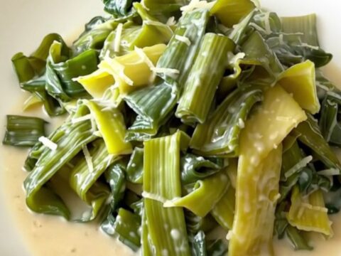 A top-down view of tender leeks in a creamy parmesan sauce inside a black slow cooker on a quartz countertop.
