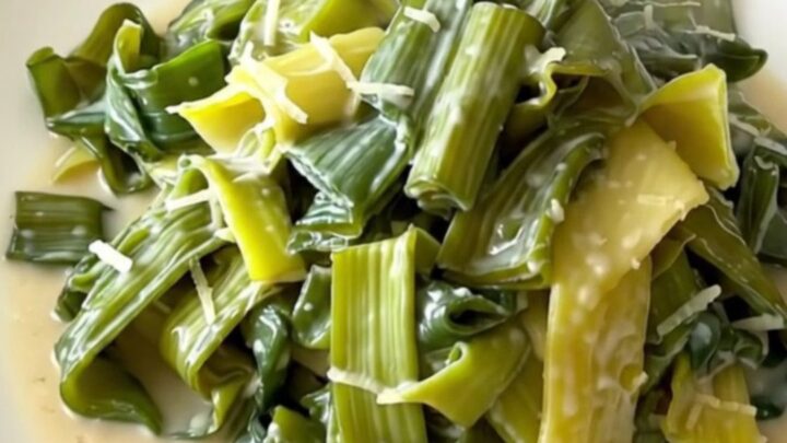 A top-down view of tender leeks in a creamy parmesan sauce inside a black slow cooker on a quartz countertop.
