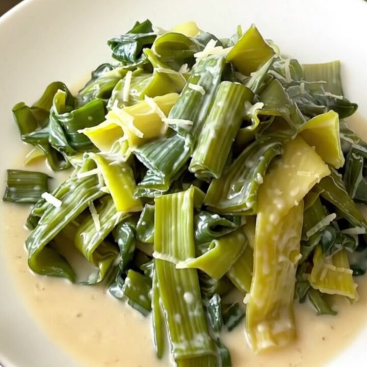 A top-down view of tender leeks in a creamy parmesan sauce inside a black slow cooker on a quartz countertop.