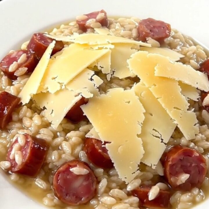 A close-up of a steaming, glossy bowl of risotto topped with melted Comté cheese and sliced sausage.