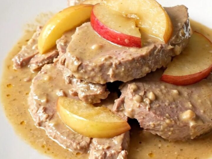 A plate of tender slow-cooked veal chunks served with apple wedges and a glossy cider sauce.