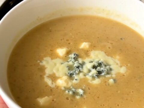A close-up of a white bowl filled with creamy, smooth parsnip and pear soup topped with blue cheese.