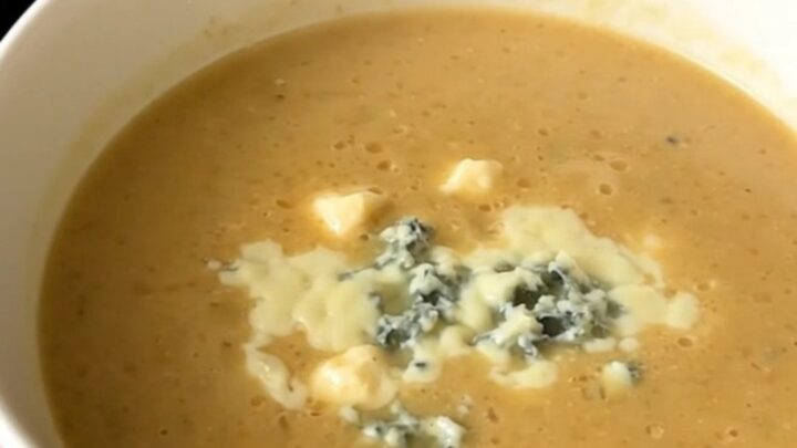 A close-up of a white bowl filled with creamy, smooth parsnip and pear soup topped with blue cheese.